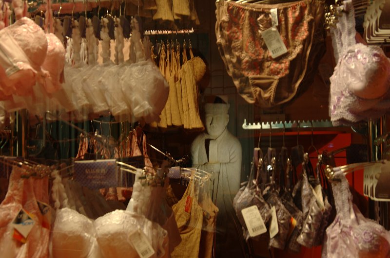 夜盲症與光 王啟瑞<br>地點：觀亭街<br/>一間賣時髦內衣的商店，雖然打佯了但商品的燈光沒有熄掉，對街的佛像映在玻璃櫥窗上，形成有意思的畫面。<br/>