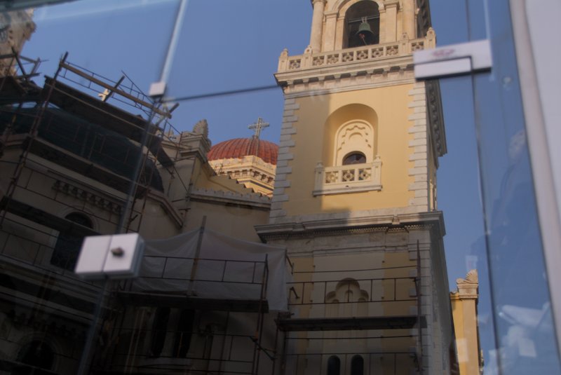 Iraklion 伊拉克里翁<br>商店玻璃櫥窗反映出，聖馬可斯教堂Agios Markos的鐘塔。<br/>